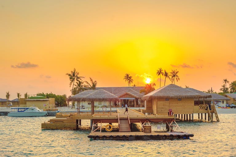 Beautiful sunset view at Kanuhura, Maldives with overwater bungalows and serene ocean surroundings.